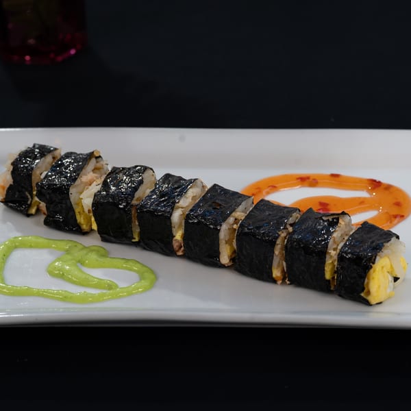 Breakfast sushi rolls with egg and rice, garnished with green and orange sauces on a white plate.