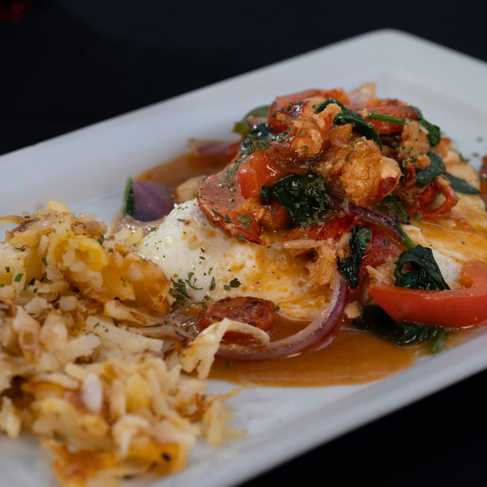 Truth Restaurant's breakfast dish with eggs, hash browns, tomatoes, spinach, and lobster on a white plate.