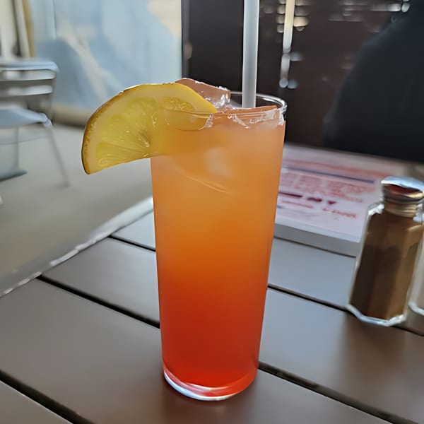 A tall glass of orange and red layered drink with ice, a straw, and a lemon slice.