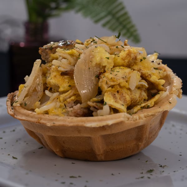 Breakfast scramble with eggs, onions, and rice, served in a waffle bowl on a white plate.