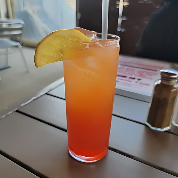 A tall glass of orange and red layered drink with ice, a straw, and a lemon slice.